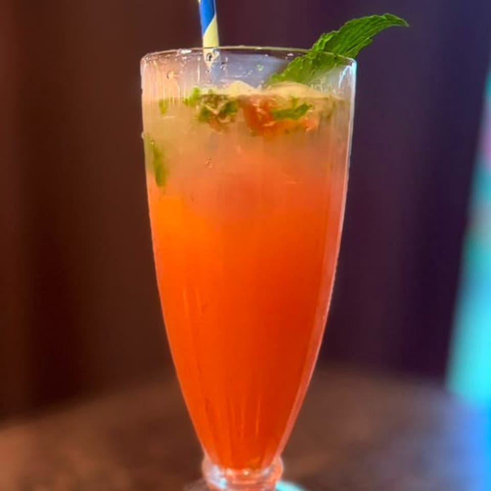 A vibrant orange cocktail with mint and a striped straw in a tall glass on a dark surface.