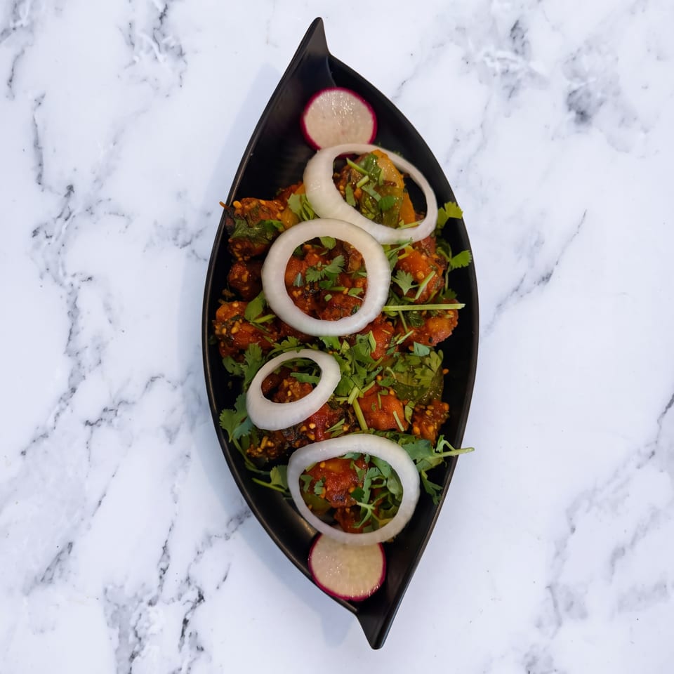 Spicy chicken dish garnished with fresh cilantro, onion rings, and radish slices on a black plate.