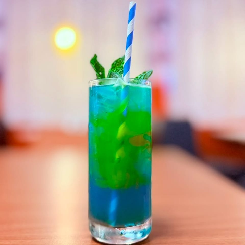 Vibrant blue and green layered cocktail with mint and a striped straw on a wooden table.